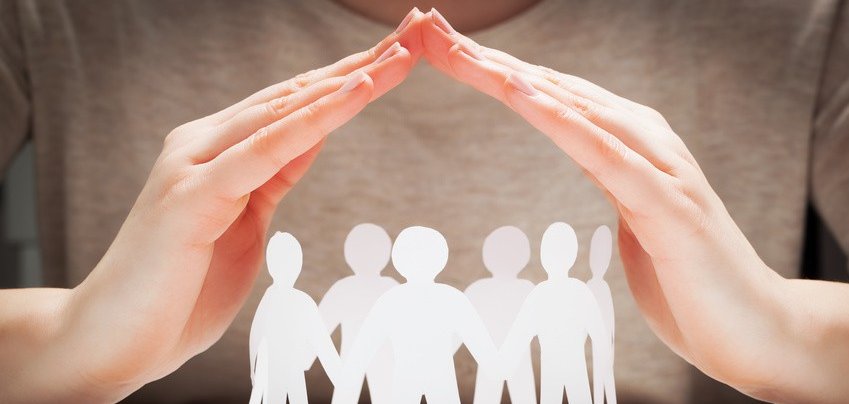 Hände schützend über Papiermenschen.