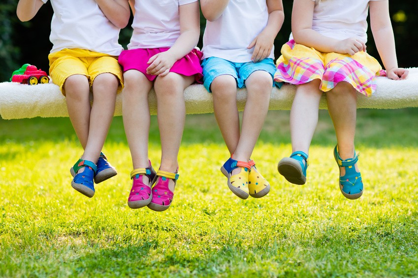 Kinder mit bunten Schuhen. Eine Gruppe von Vorschulkindern mit bunten Schuhen auf einem Ast lassen ihre Füße ins Bild baumeln.
