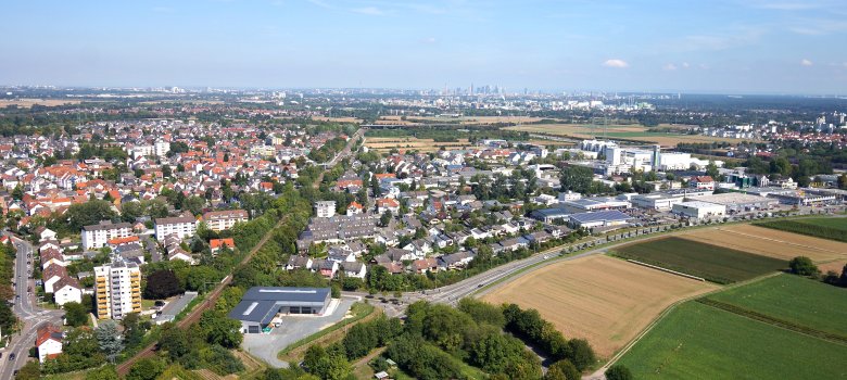 Kriftel aus der Vogelperspektive: Dächer des Wohngebiets sind zu sehen und der Blick geht bis zur Skyline Frankfurts am Horizont.