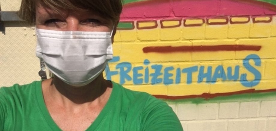 Lydia Rauh mit Maske vor einem Graffitti mit dem Wort Freizeithaus.