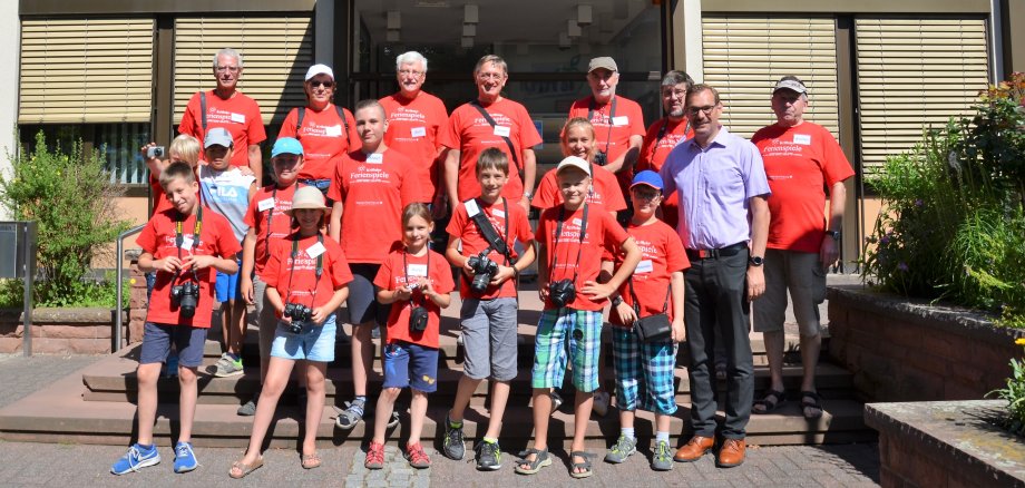 Kinder mit roten Ferienspiel-Tshirts und Kameras vor dem Rat- und Bürgerhaus.