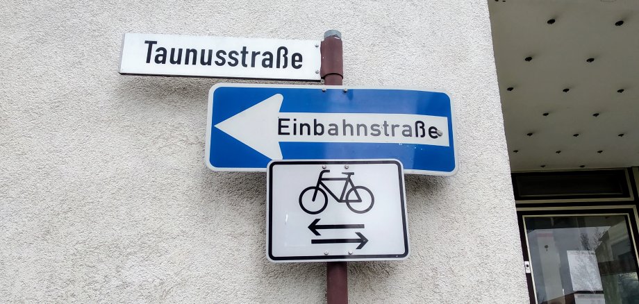 Ein Straßenschildmit dem Hinweis auf die Einbahnstraße und in beide Richtungen fahrende Radfahrer.