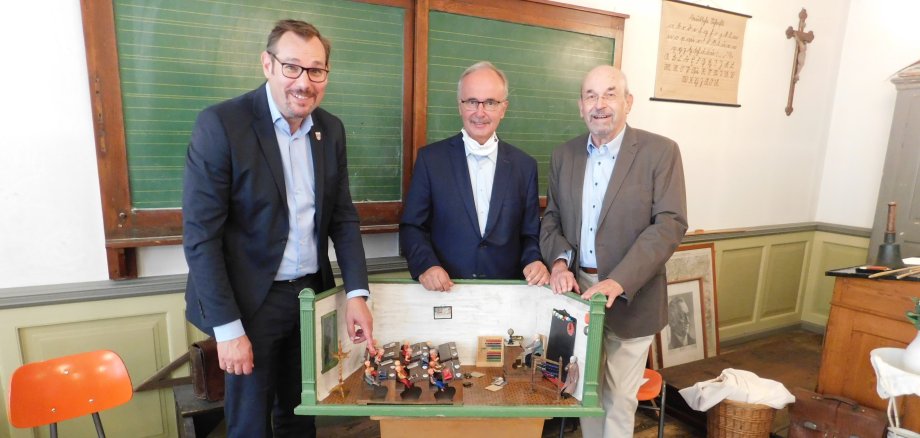 Bürgermeister Seitz, ehemaliger Schuldezernent Kollmeier und Schulmuseumsleiter Janecke stehen hinter der neuen Puppenstube.