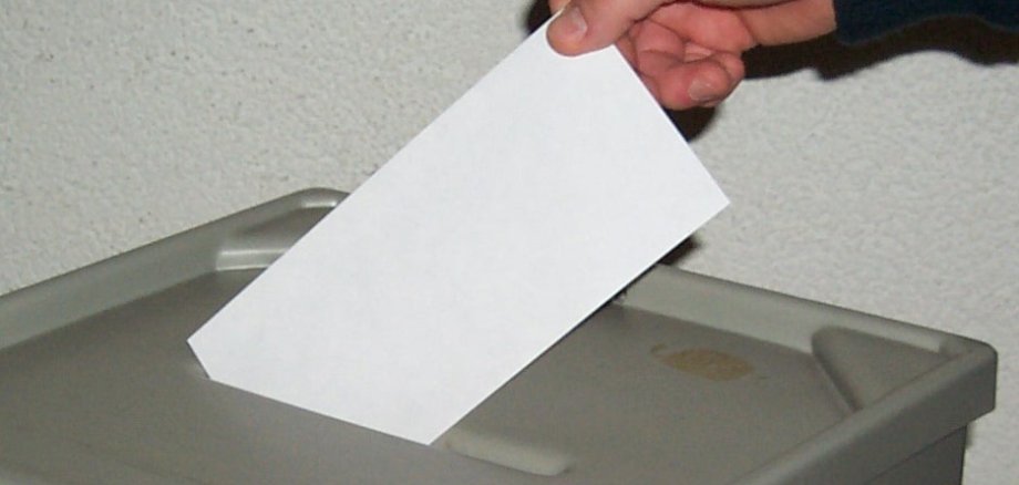 Eine Hand wirft einen Stimmzettel in die Wahlurne.