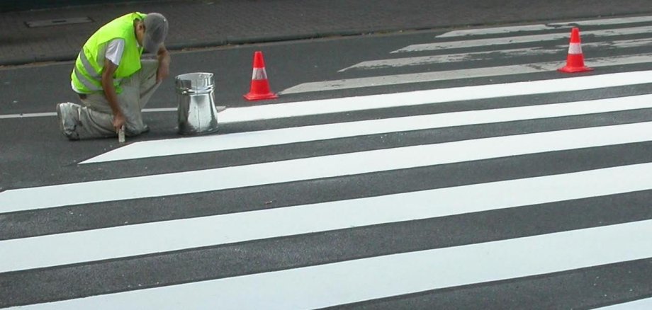Ein Arbeiter malt einen Zebrastreifen auf die Straße.