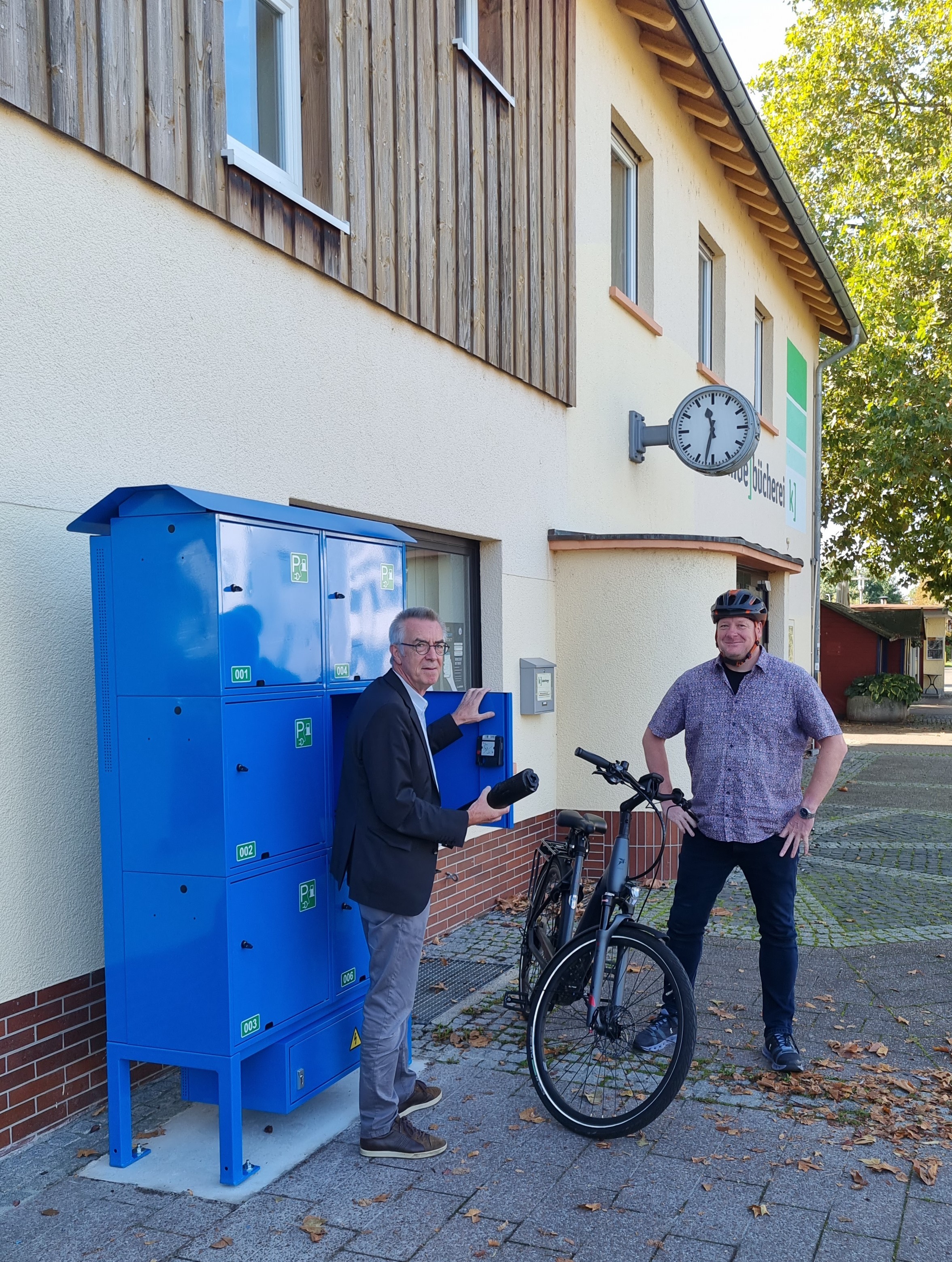Jirasek und Schwarz mit E-Bike vor einem offenen Schließfach.