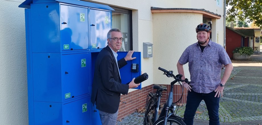 Jirasek und Schwarz mit E-Bike vor einem offenen Schließfach.