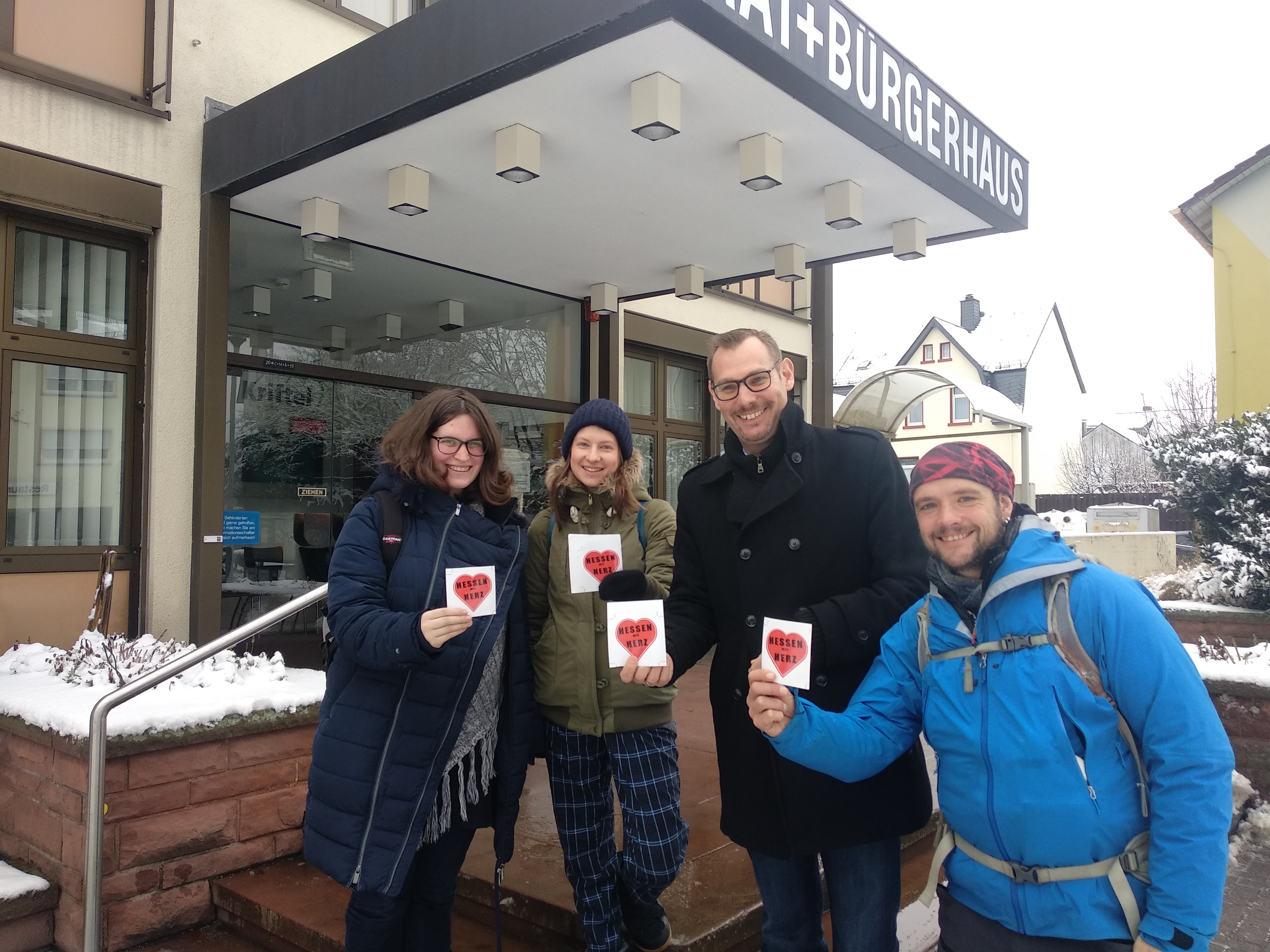Eva und Lars mit Bürgermeister Seitz vor dem Rathaus. Alle halten einen Herz-Aufkleber in die Höhe.