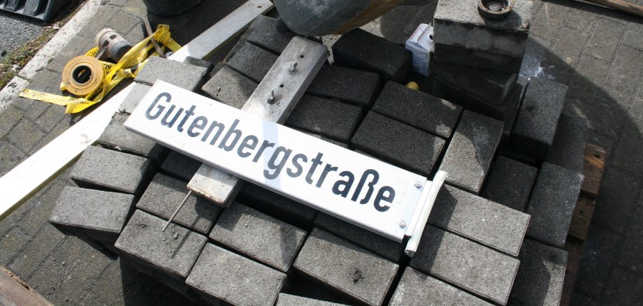 Ein Straßenschild mit der Aufschrift Gutenbergstraße liegt auf Pflastersteinen.