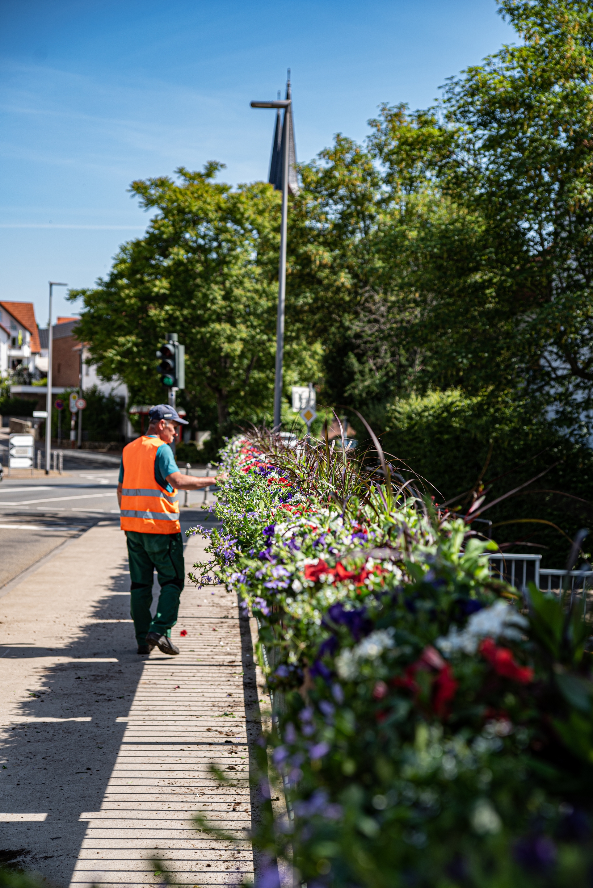 Ein Mitarbeiter den Bauhofes vor den neubepflanzten Blumenkästen am Brückengeländer. Hinten sieht man die Kirchturmspitze.