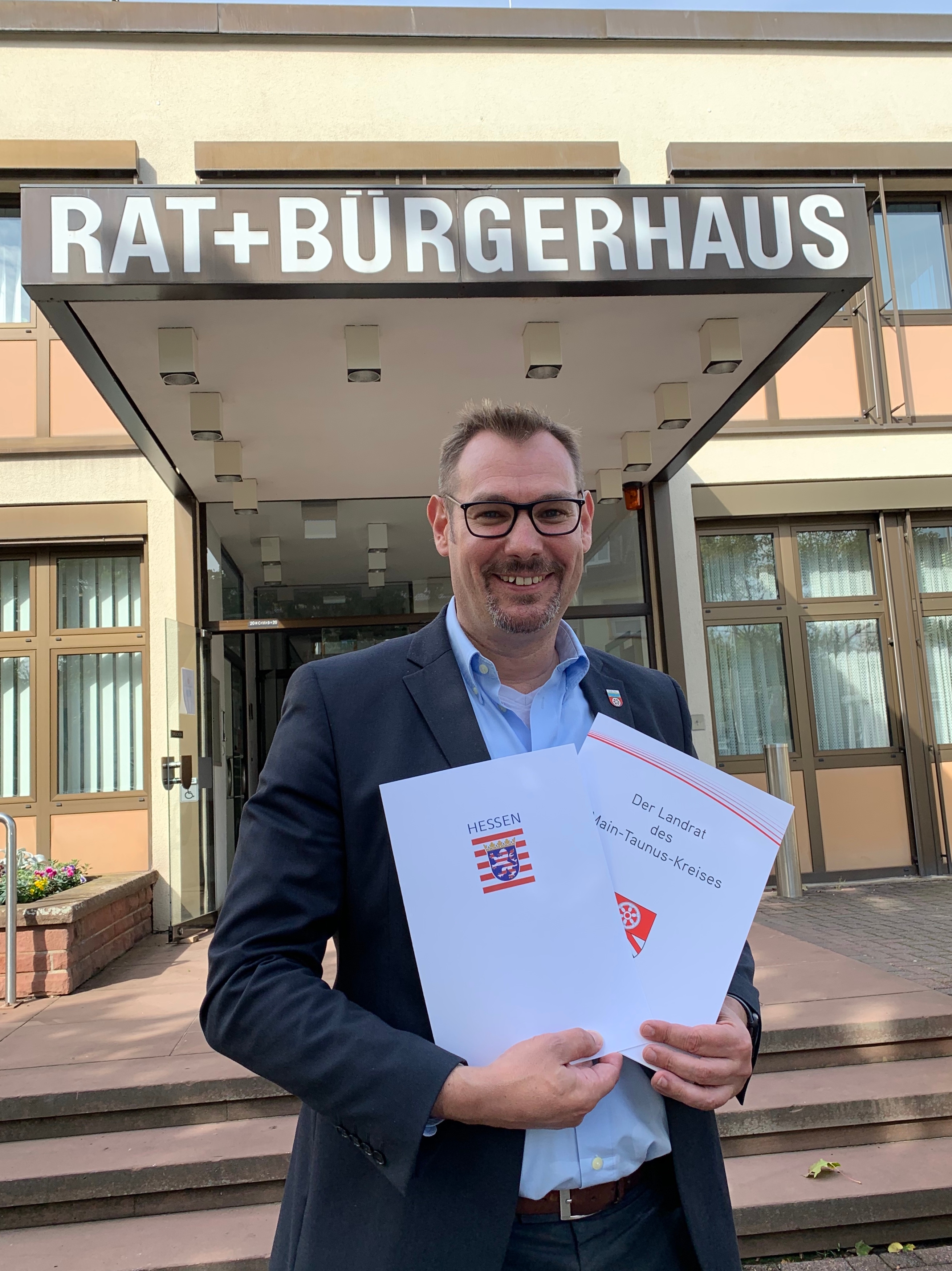 Bürgermeister Seitz vor dem Rathaus mit Bescheiden von Land und Kreis in der Hand.
