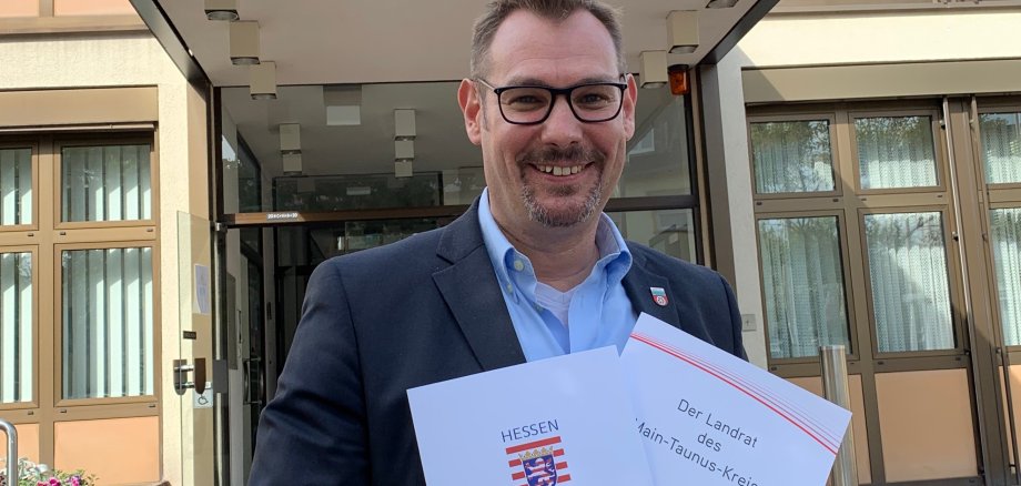 Bürgermeister Seitz vor dem Rathaus mit Bescheiden von Land und Kreis in der Hand.
