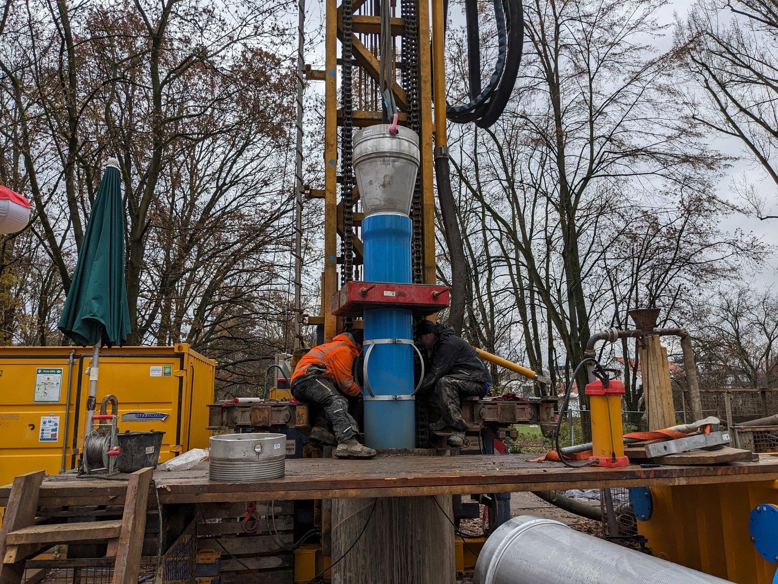 Arbeiter führen ein Rohr in den neu gebohrten Brunnenschacht ein.