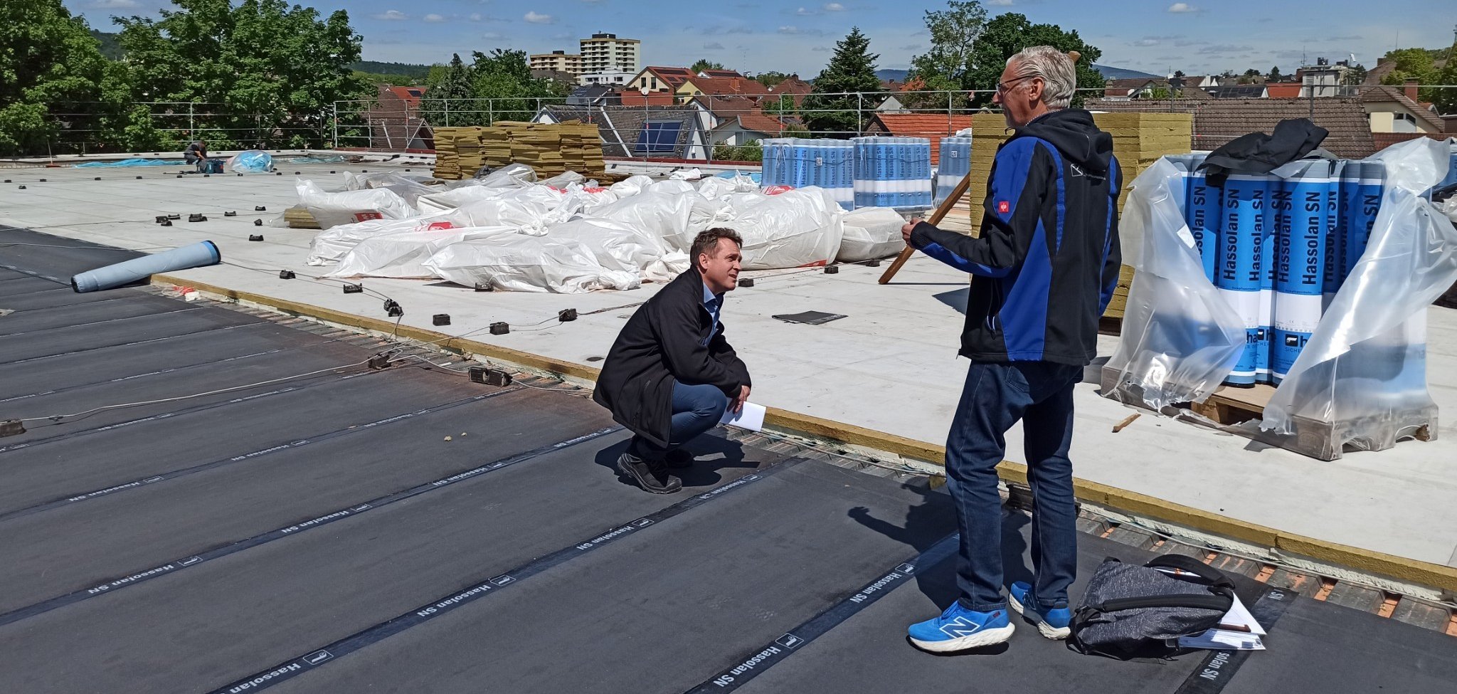 Mohr hockt auf neuer Folie auf dem Dach und der Architekt erklärt.