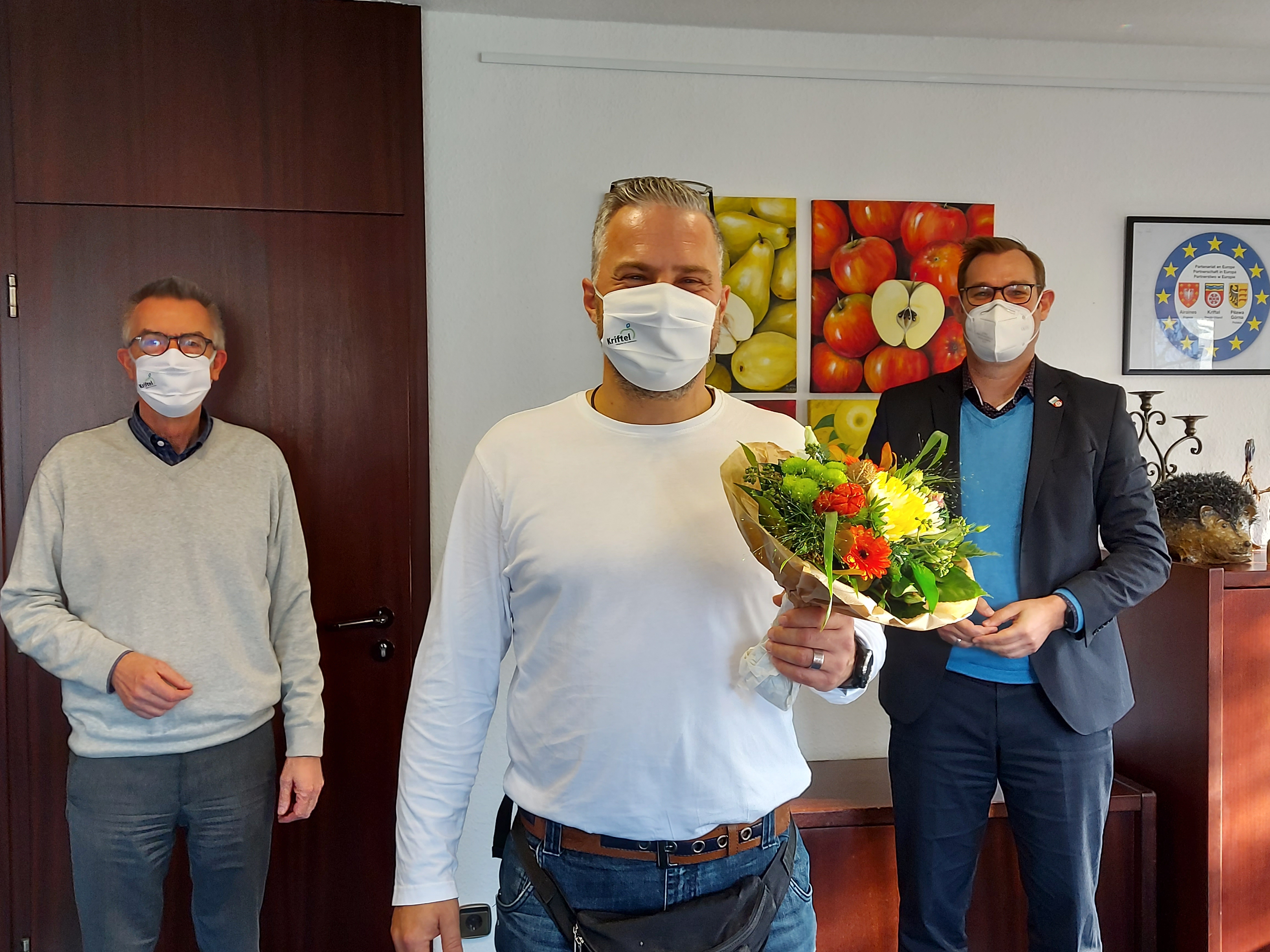 Drago Knezevic mit Blumenstrauß neben Bürgermeister Seitz und dem Ersten Beigeordneten Franz Jirasek. Alle tragen Masken.