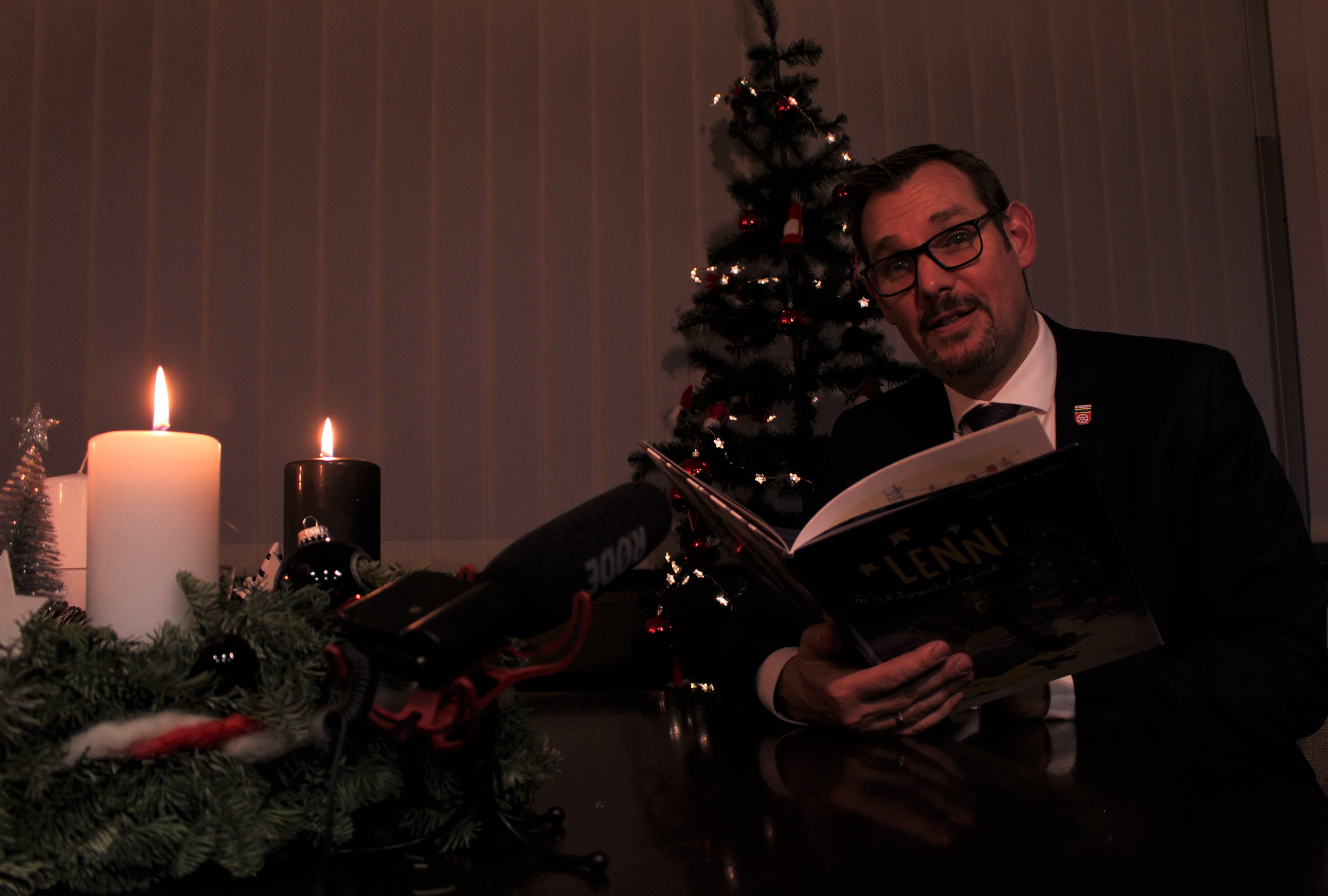 Bürgermeister Seitz mit Bilderbuch vor einem Tannenbaum in seinem Büro.