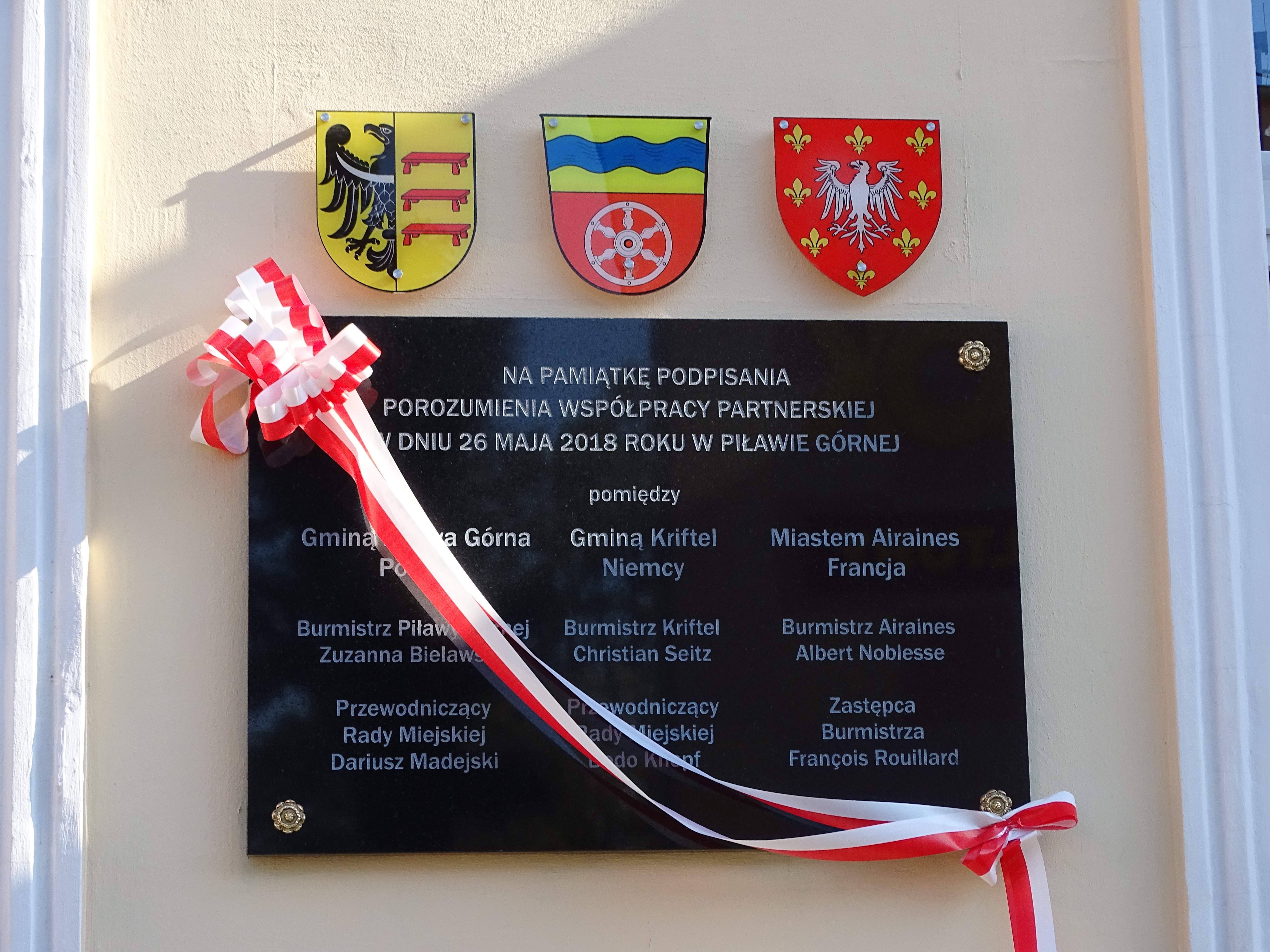 Die Gedenktafel mit den drei Wappen der drei Partnerstädte Airaines, Kriftel und Pilawa Gorna.