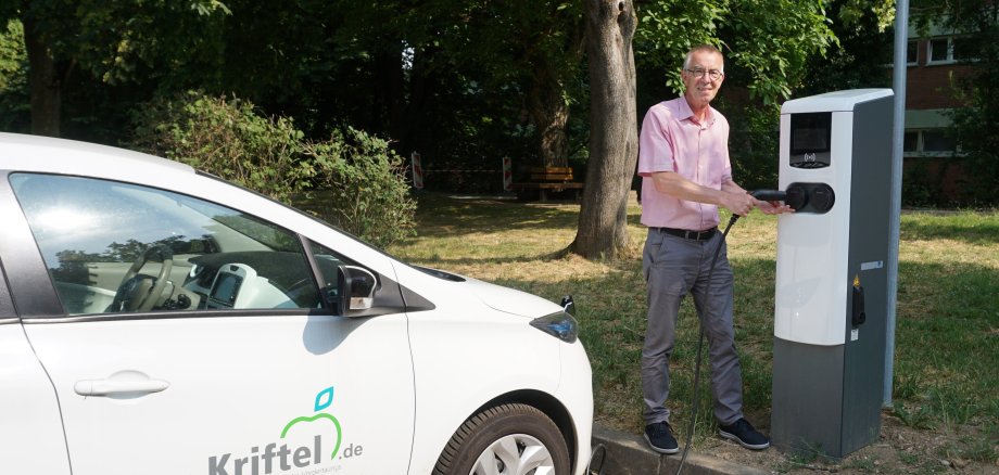 Jirasek mit Elektroauto der Gemeinde vor neuer Ladesäule an der Schwarzbachhalle.