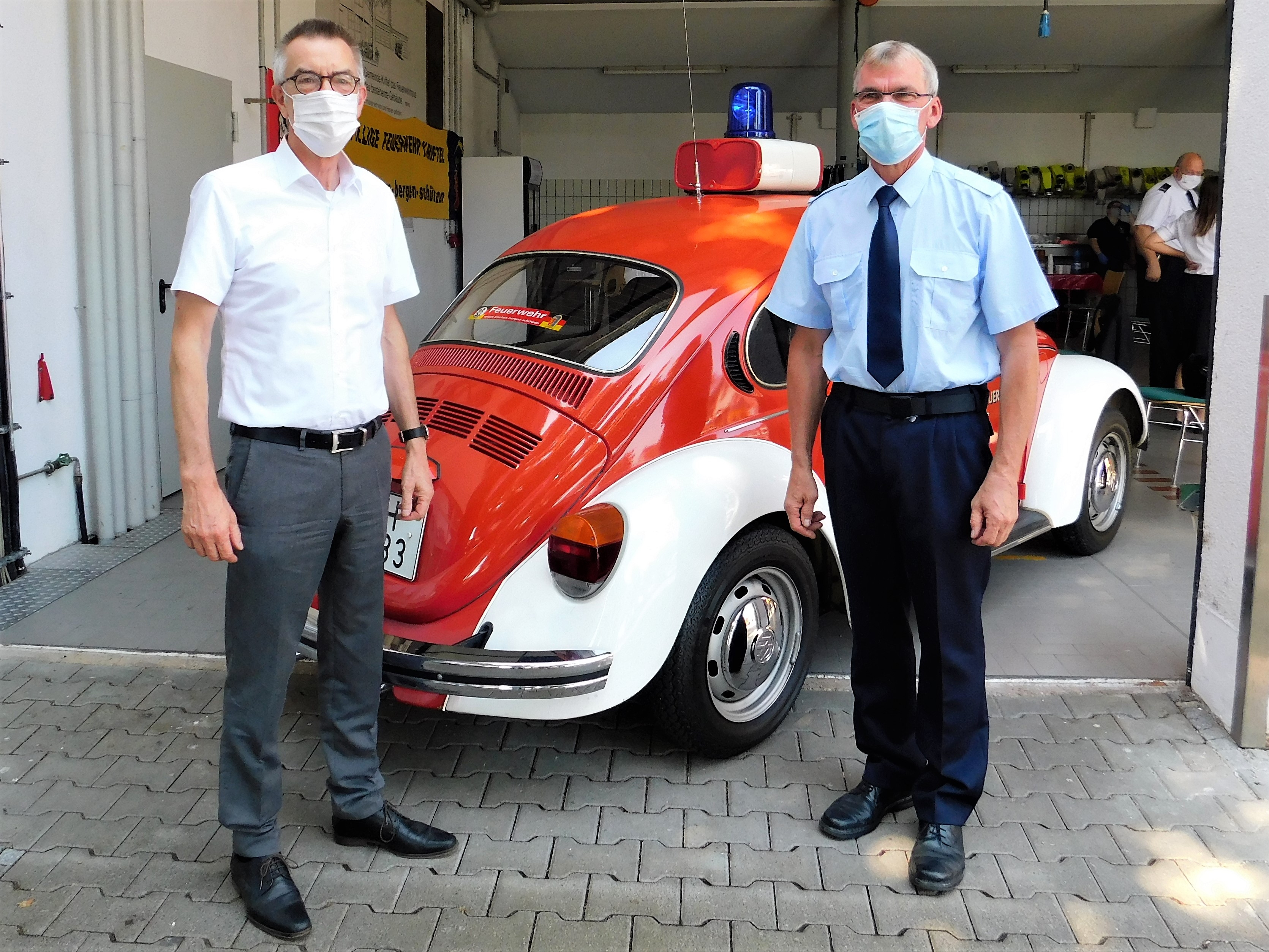 Der Erste Beigeordnete Franz Jirasek mit Werner Hasel vor einem Feuerwehrfahrzeug. Beide tragen Mundschutz.