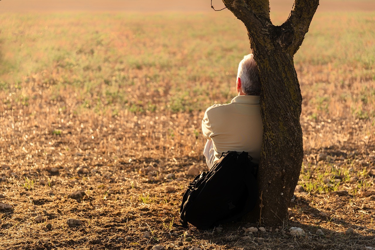 Ein Mann sitzt auf dem Boden an einen Baum gelehnt.