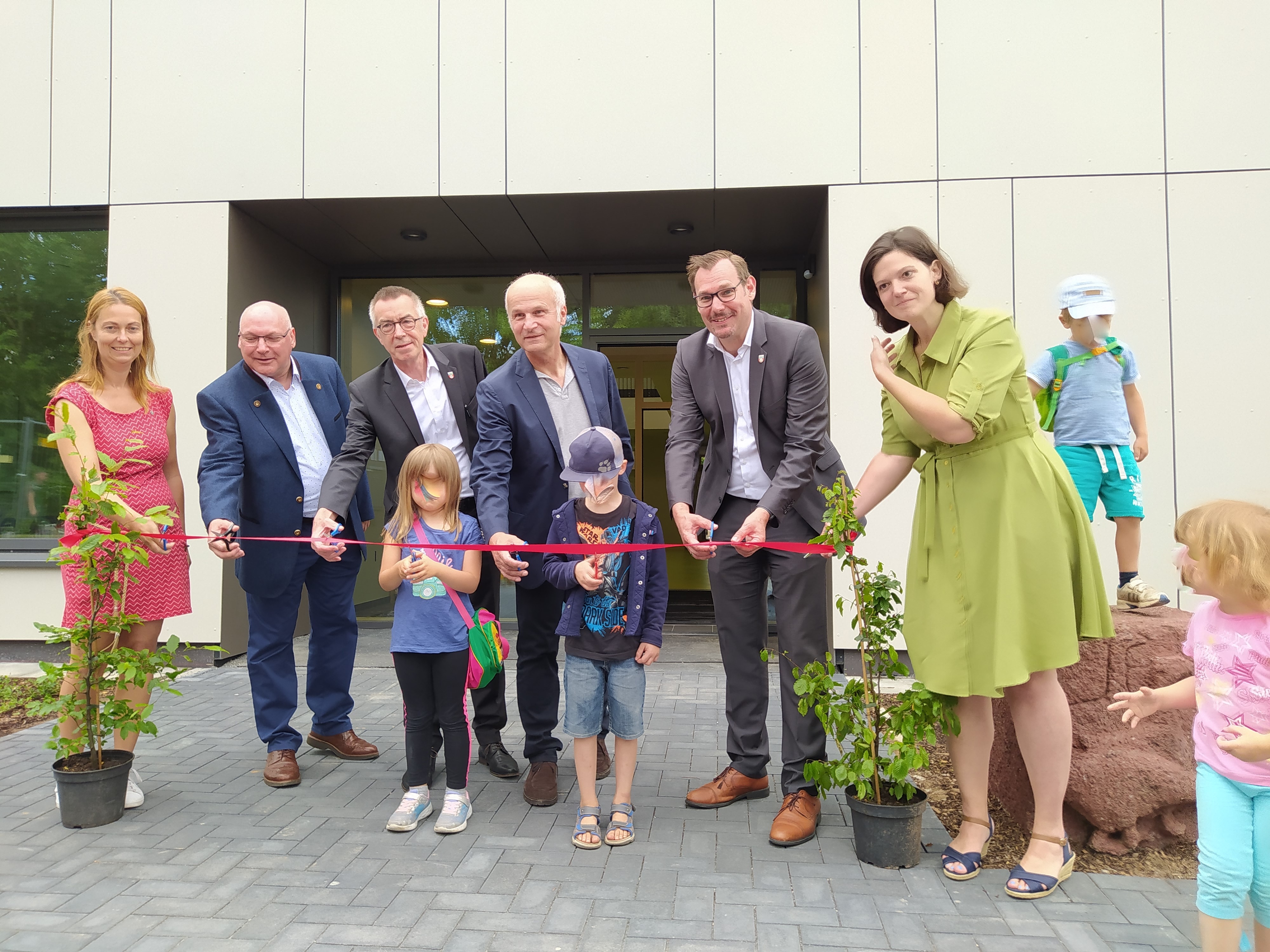 Offizielle und Kinder durchschneiden symbolisch das rote Band vor der neuen Kita..