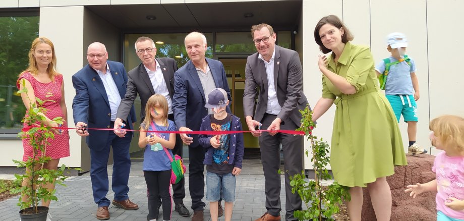Offizielle und Kinder durchschneiden symbolisch das rote Band vor der neuen Kita..