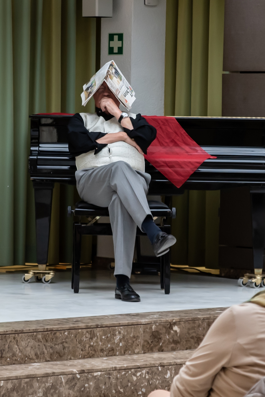 Dietmar Vollmert mit Zeitung auf dem Kopf lehnt am Klavier.