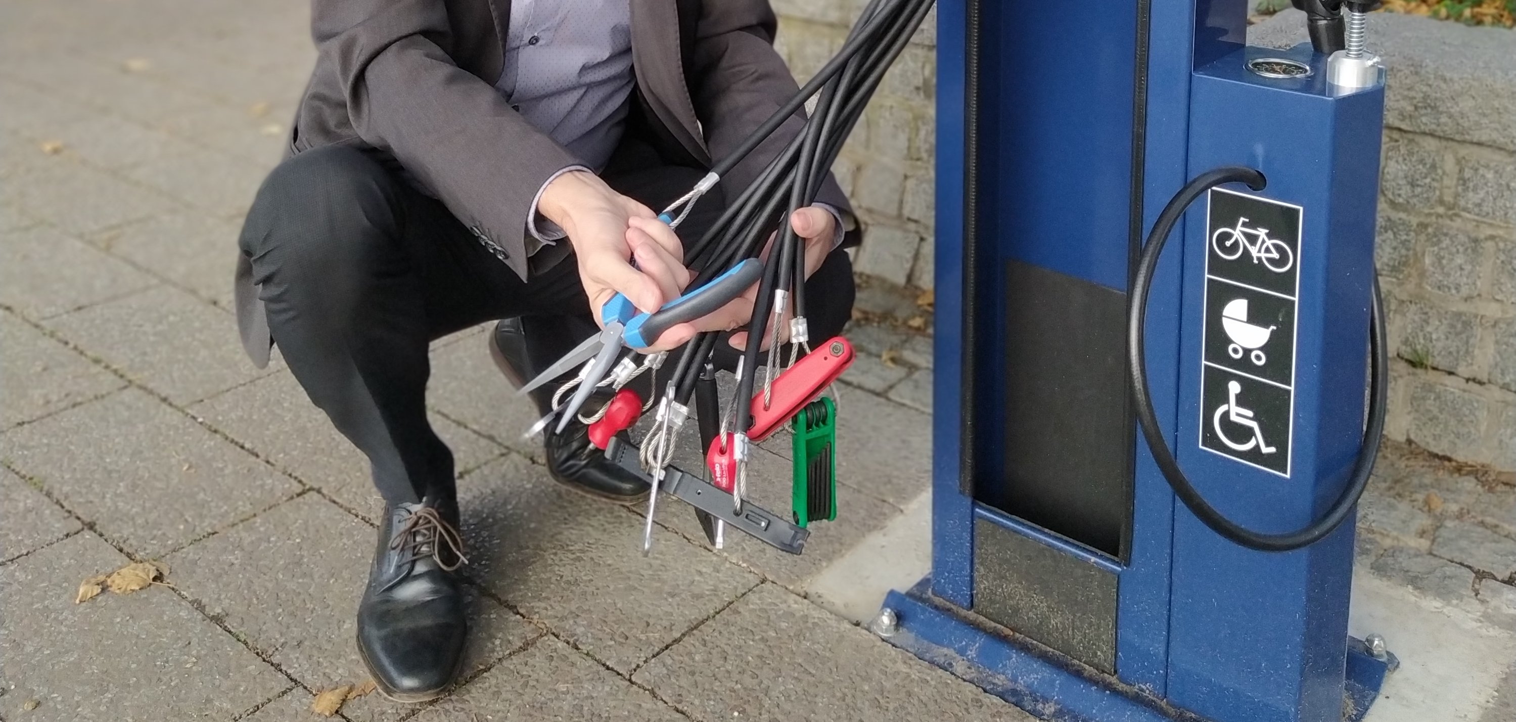 Franz Jirasek hockt neben der Station und zeigt die Werkzeuge, die an Drähten befestigt sind und so nicht gestohlen werden können.