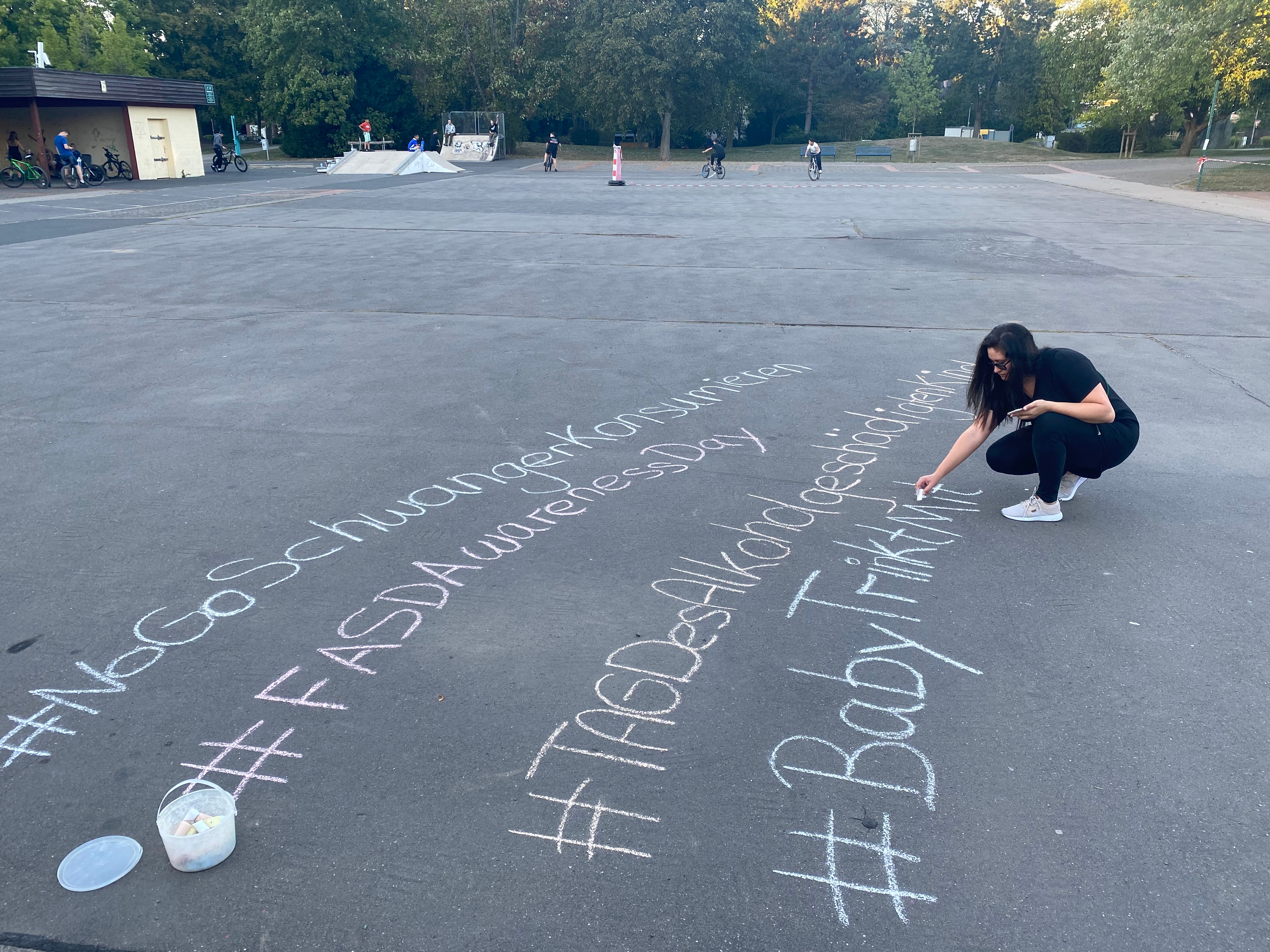 Eine Frau schreibt mit Kreide Schriftzüge gegen Alkohol in der Schwangerschaft auf den Festplatz im Freizeitpark.