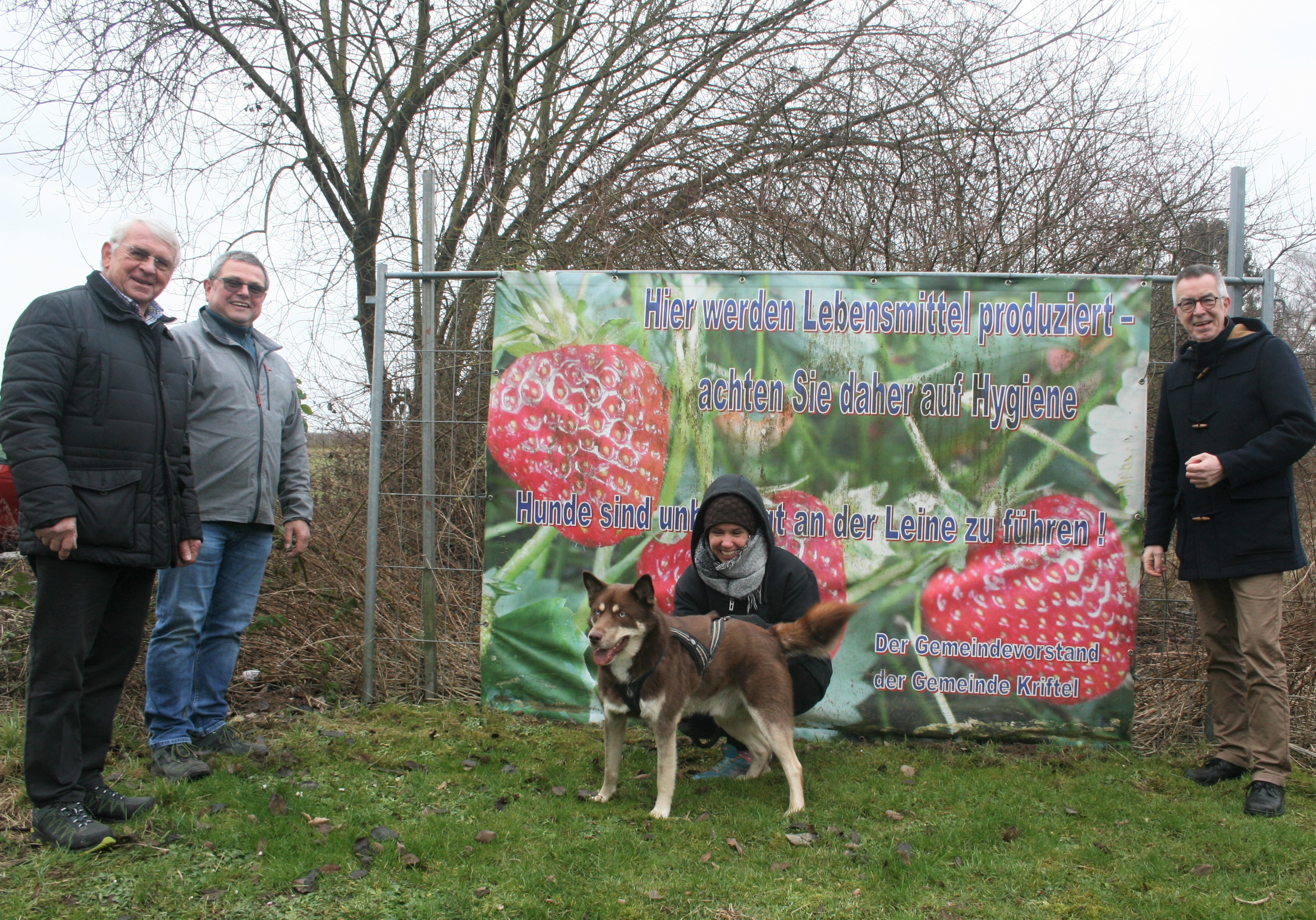 Jirasek, Hoss und Theis vor einem Banner. Eine Spaziergängerin mit Hund kniet davor.