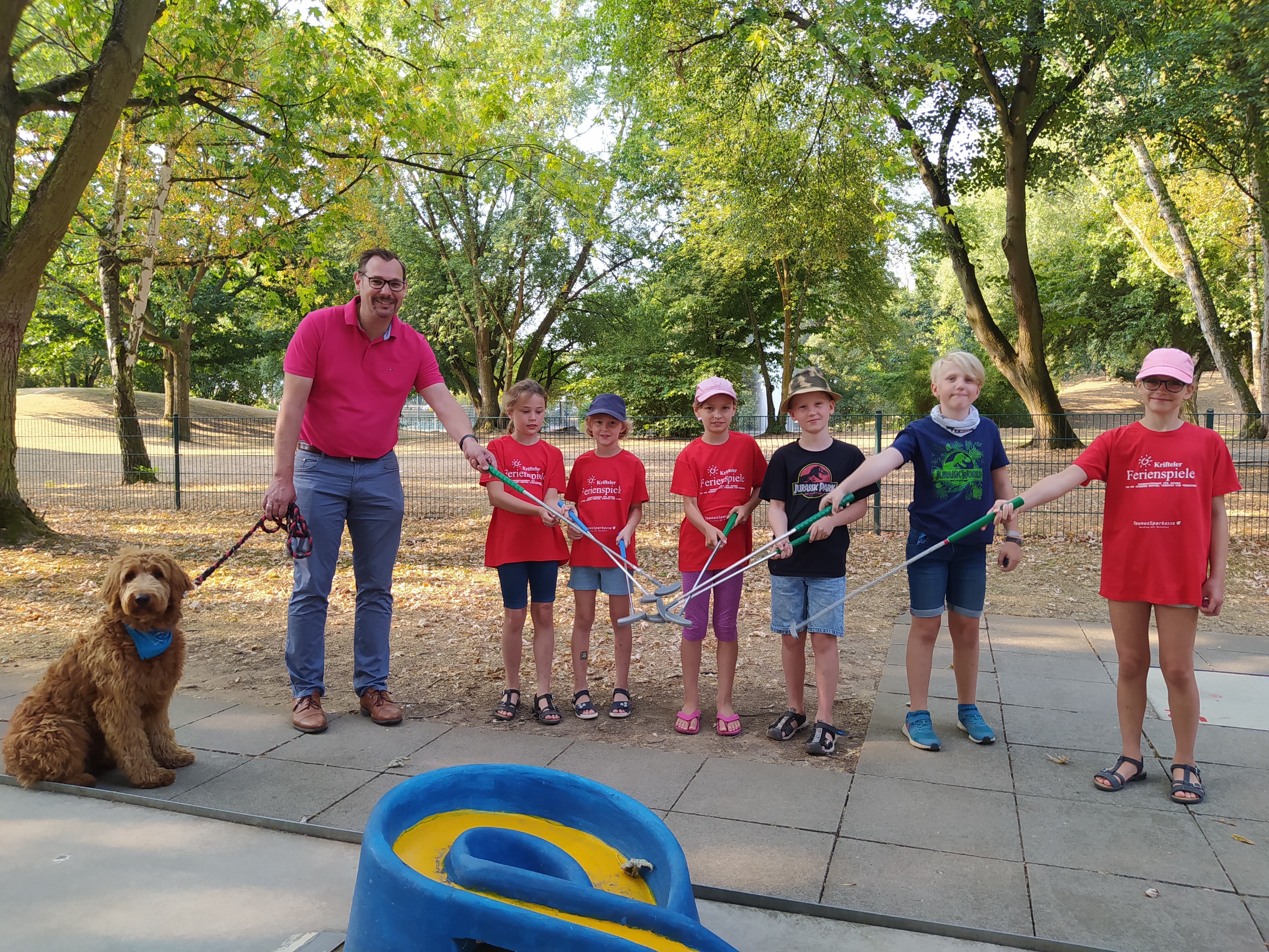 Bürgermeister mit Hund Bailey und sechs Kinder auf dem Minigolfplatz. Sie halten ihre Schläger aneinander.
