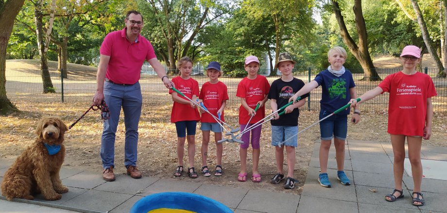 Bürgermeister mit Hund Bailey und sechs Kinder auf dem Minigolfplatz. Sie halten ihre Schläger aneinander.