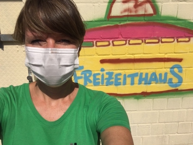 Lydia Rauh mit Maske vor einem Graffitti mit dem Wort Freizeithaus.