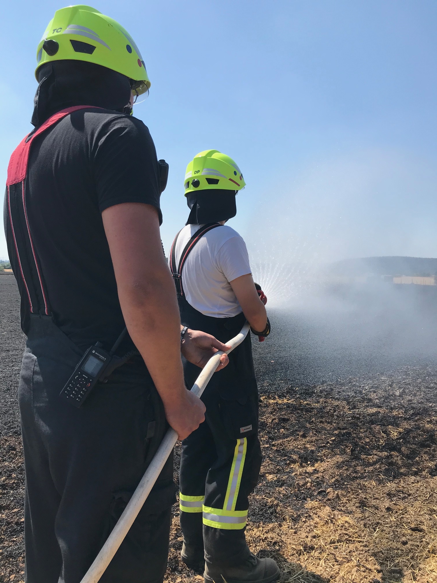 Zwei Wehrleute mit Schlauch löschen einen Feldbrand.