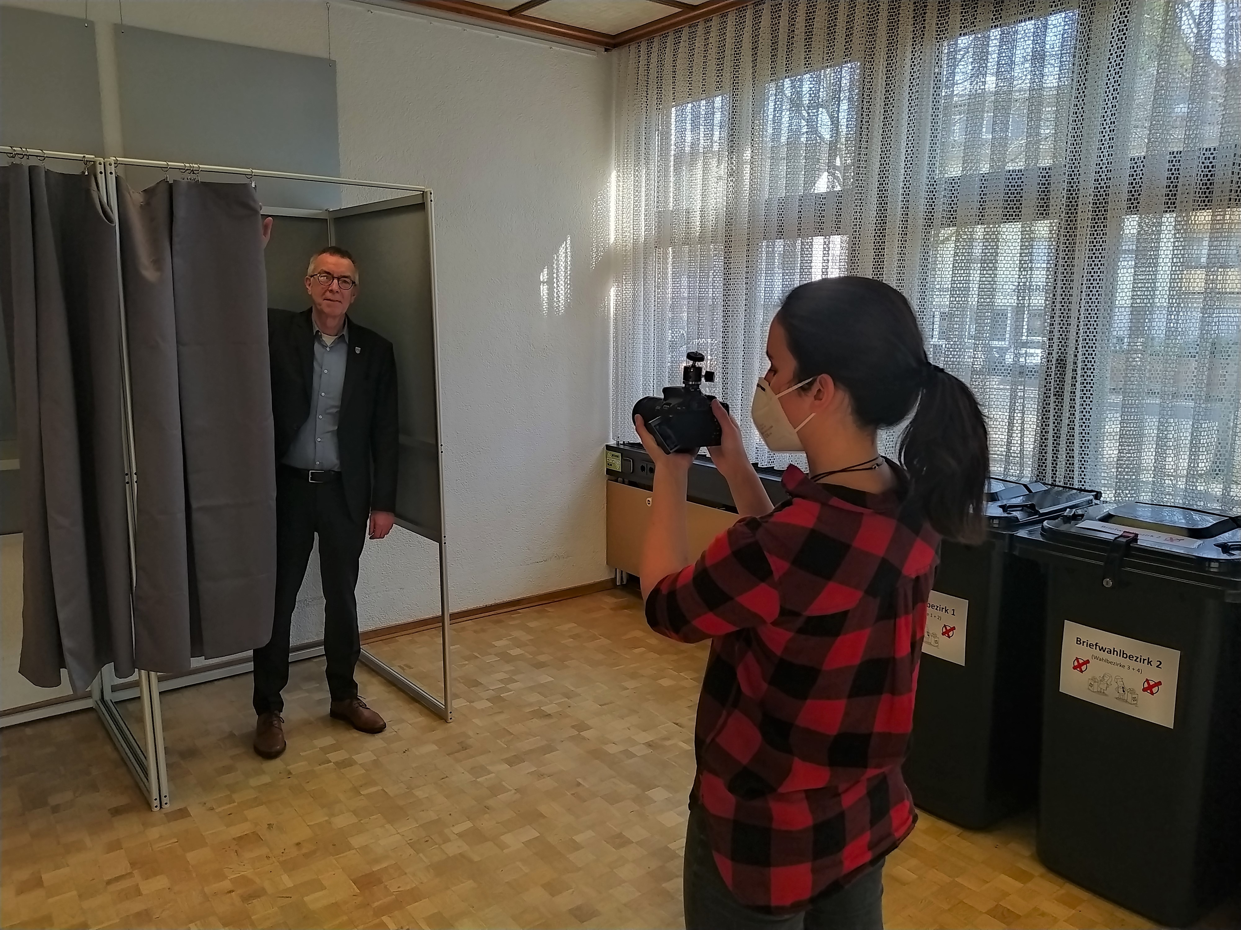Franz Jirasek steht in der Wahlkabine. Davor die Filmerin mit Kamera.