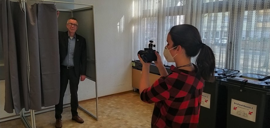 Franz Jirasek steht in der Wahlkabine. Davor die Filmerin mit Kamera.