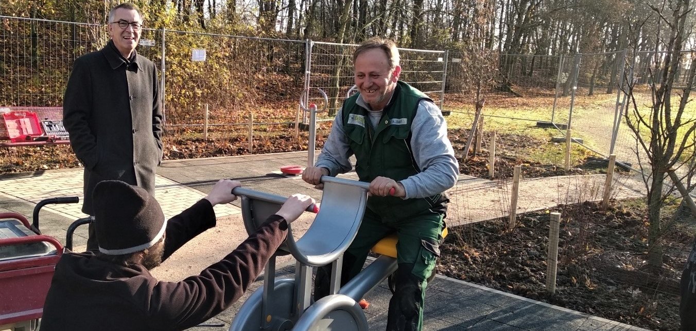 Zwei Bauarbeiter schaukeln auf einem neuen Fitnessgerät. Der Erste Beigeordnete Franz Jirasek lacht.