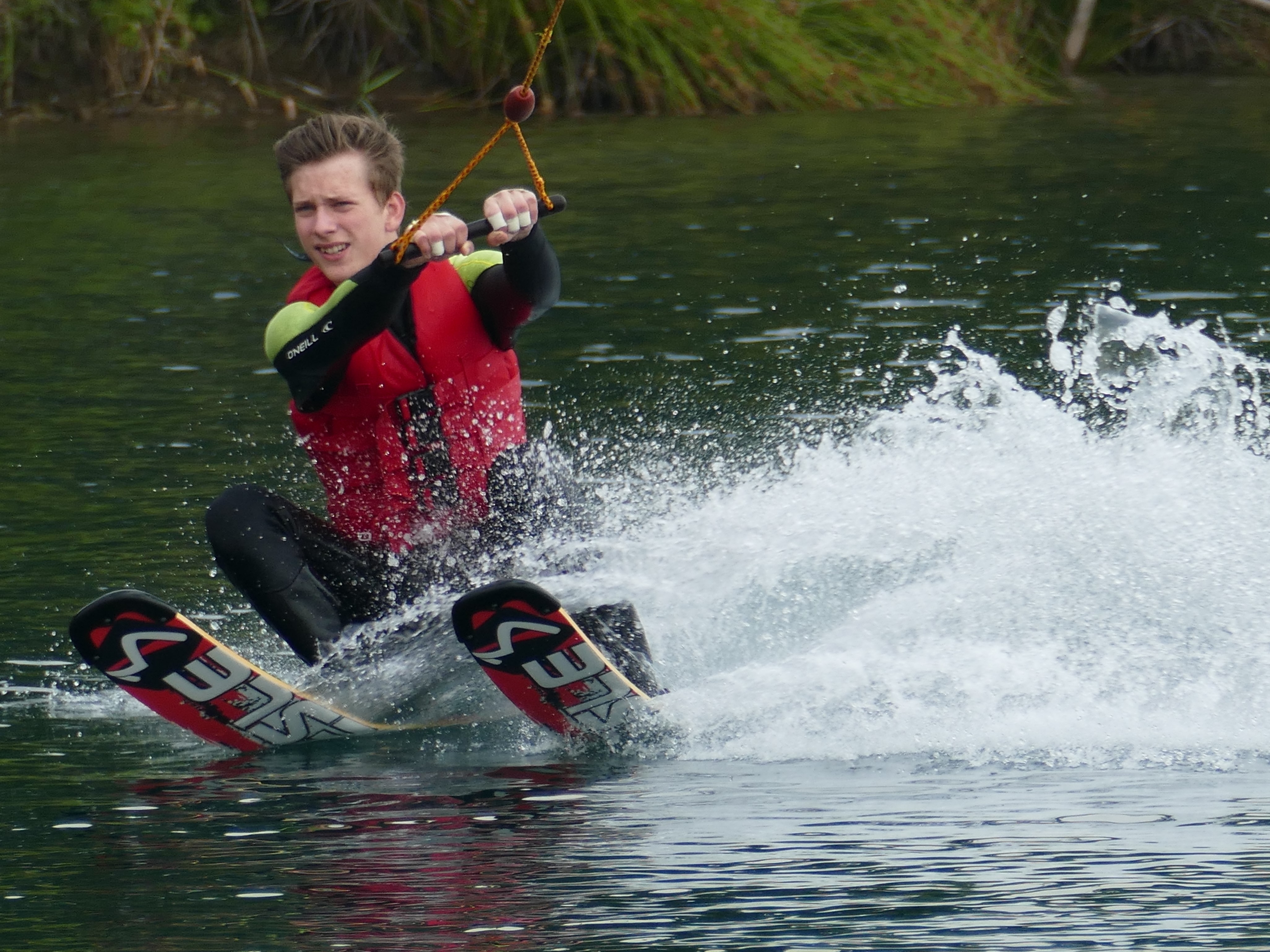 Ein Junge wird auf Wasserskiern durchs Wasser gezogen. Wasser spritzt.