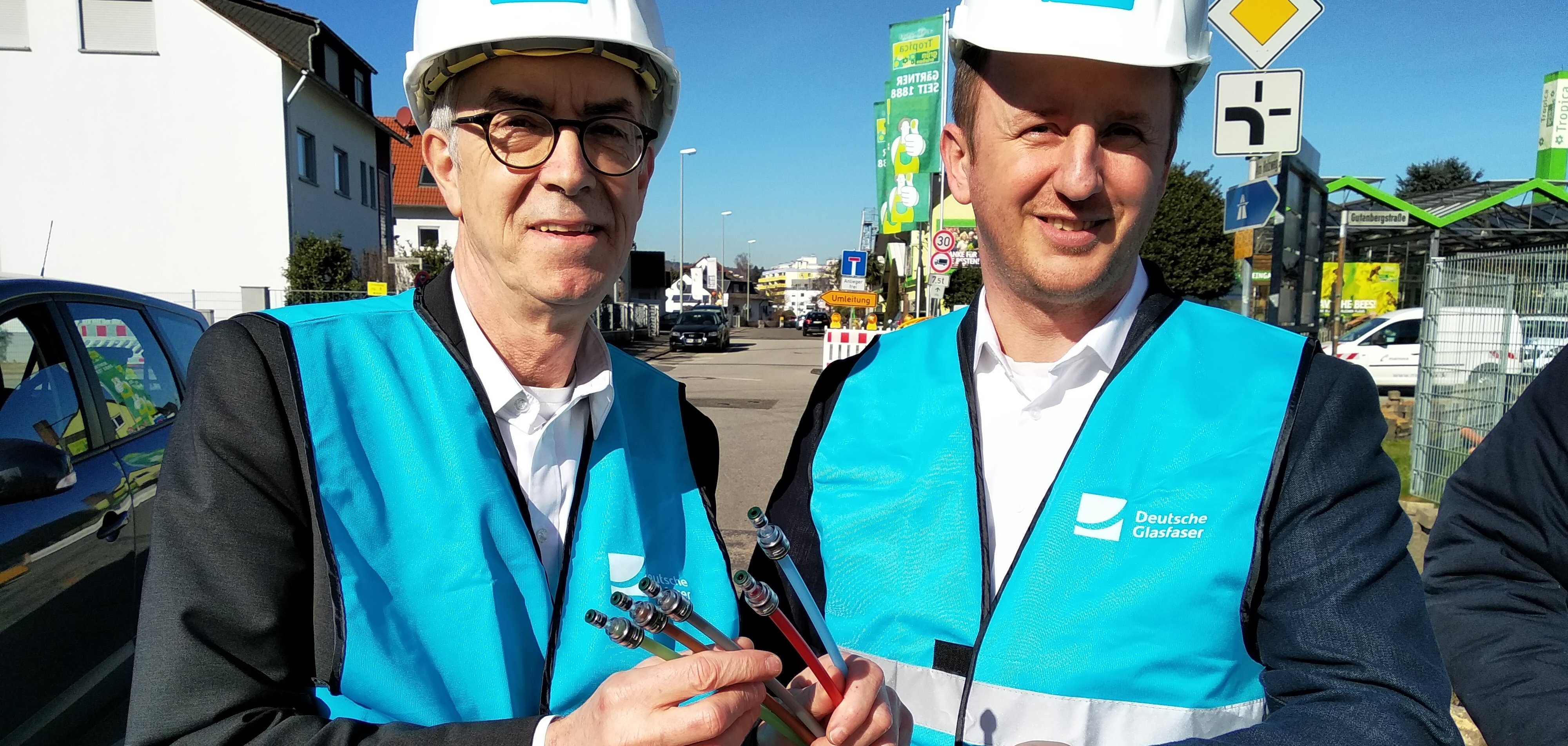 Franz Jirasek und ein Vertreter der Dutsche Glasfaser mit Helm und Glasfaserkabeln auf der Baustelle.