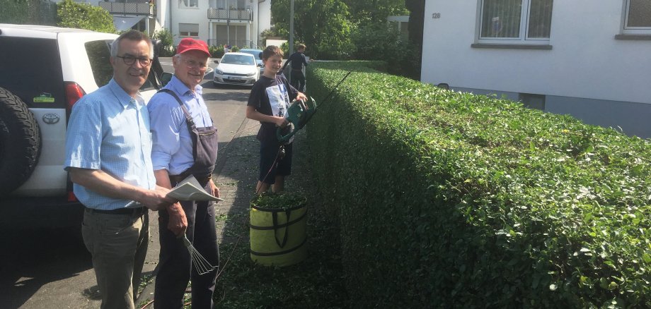 Der Erste Beigeodnete im Gespräch mit einem Bürgere, der gerade mit seinem Sohn seine Hecke schneidet.