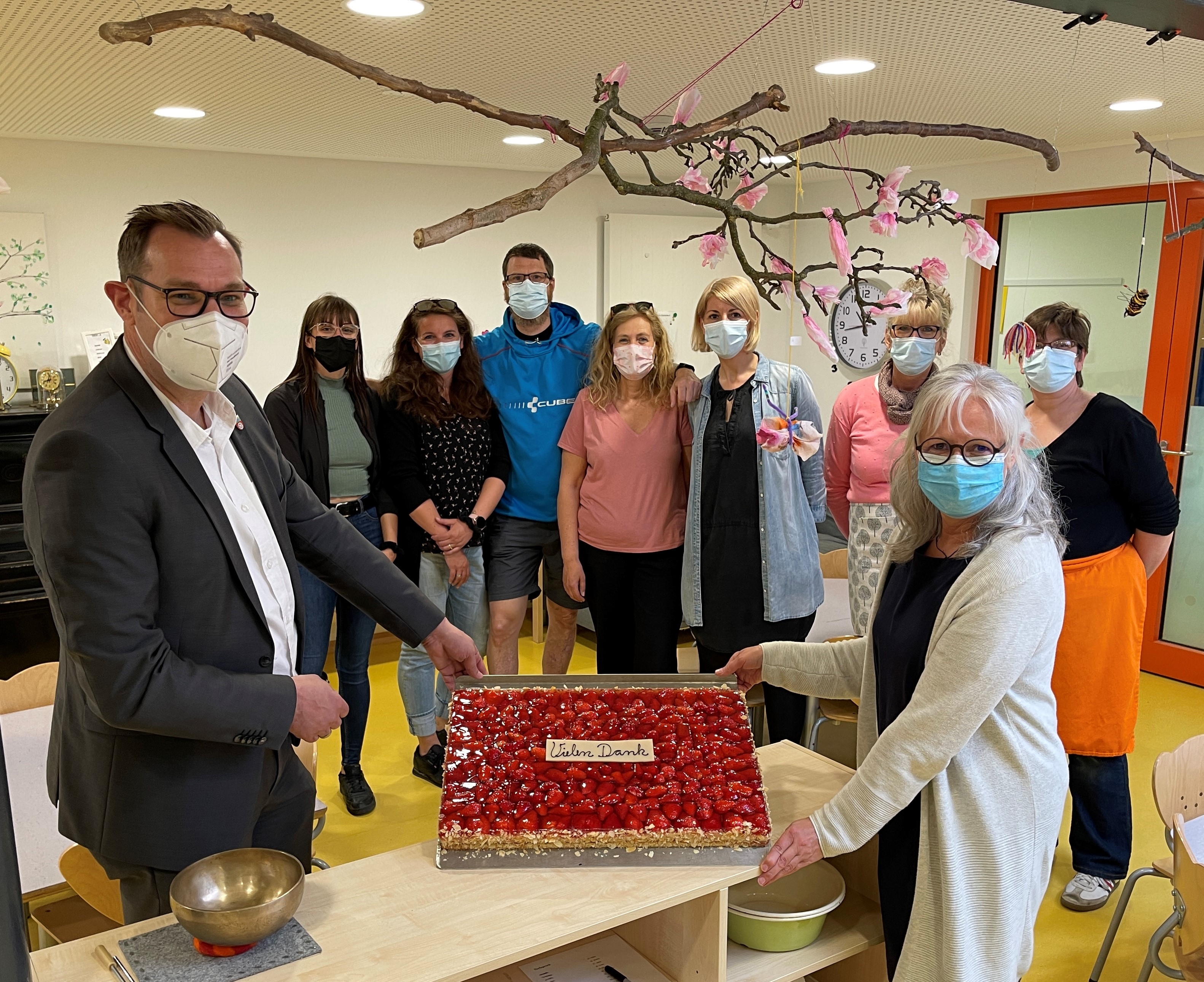 Bürgermeister Seitz übergibt ein Blech Erdbeerkuchen an das Team der Kita Obstgärtchen.