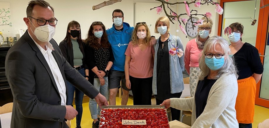 Bürgermeister Seitz übergibt ein Blech Erdbeerkuchen an das Team der Kita Obstgärtchen.
