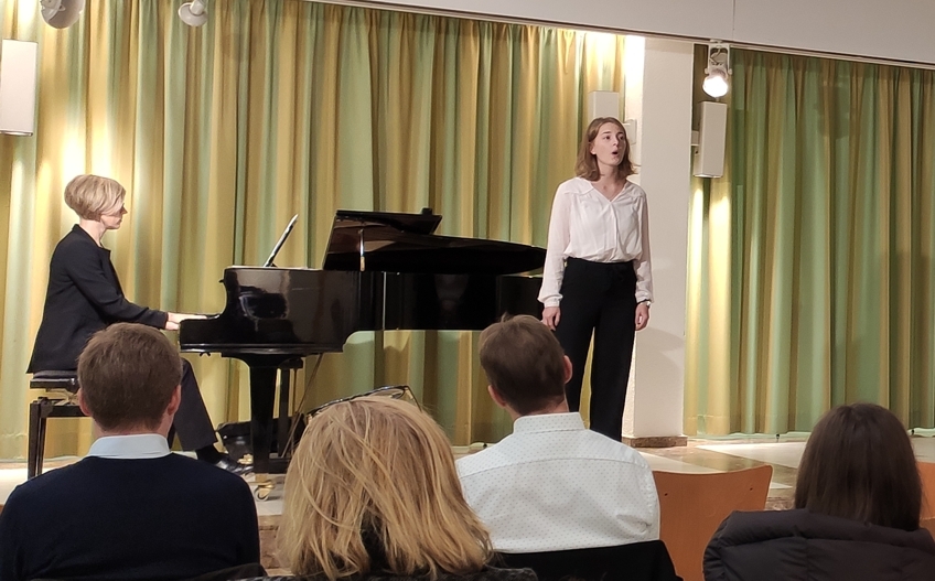 Eine Sängerin auf der Bühne neben dem Klavier.