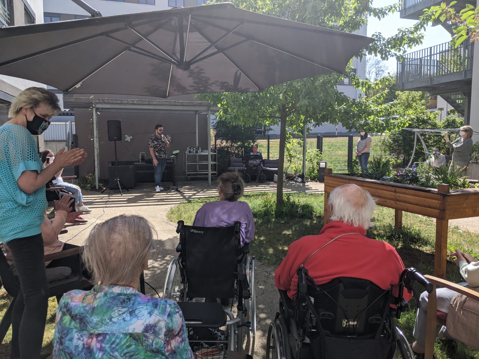 Giovanni LOmbardo singt im Garten, Menschen in Rollstühlen hören zu,