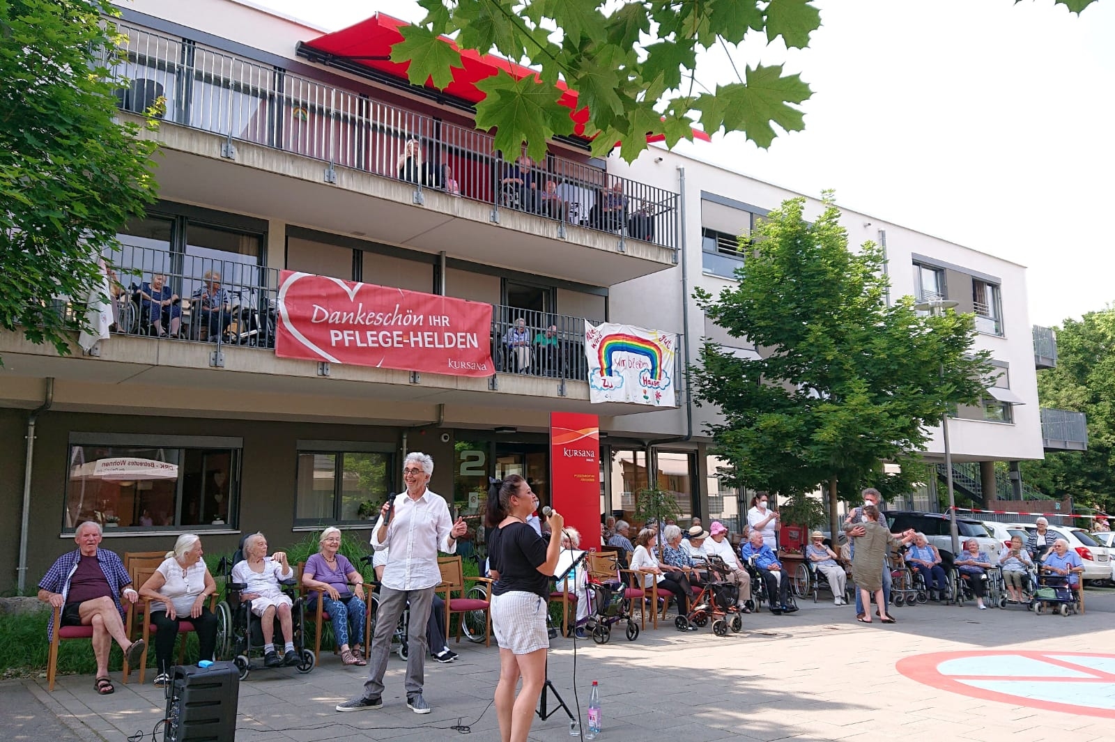 Lorth und Gorol mit Mikrofonen vor dem Kursana Domizil. Jede Menge Senioren sitzen auf den Balkonen oder auf Stühlen davor.