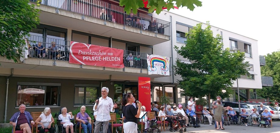 Lorth und Gorol mit Mikrofonen vor dem Kursana Domizil. Jede Menge Senioren sitzen auf den Balkonen oder auf Stühlen davor.