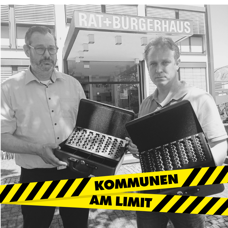 Seitz und Mohr mit ernsten Gesichtern und leeren Handkassen vorm Rathaus.