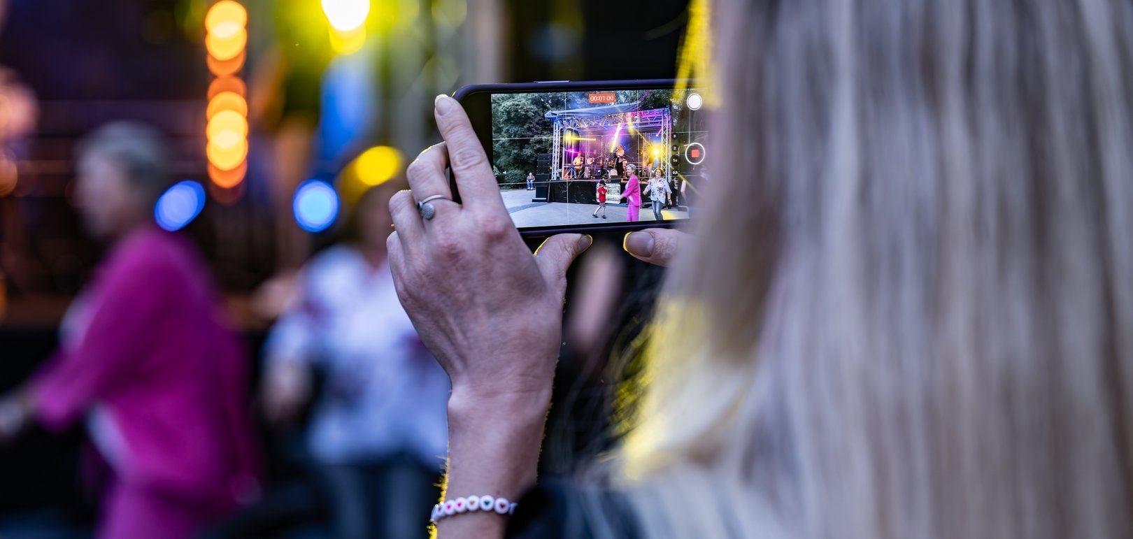 Eine Frau filmt mit dem Handy die Bühne und tanzende Besucher/innen.