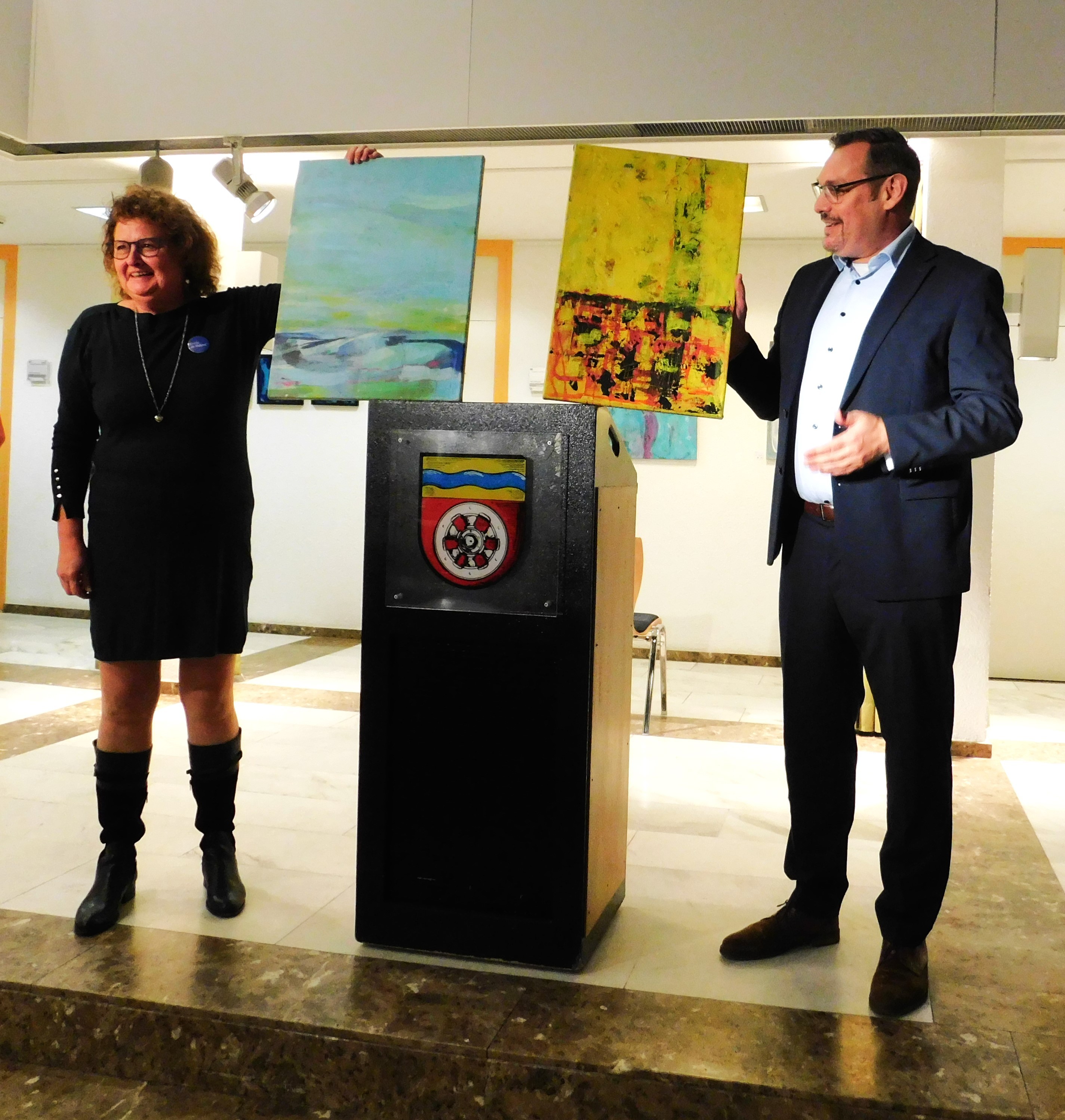 Bürgermeister und Künstlerin halten zwei Bilder hoch.