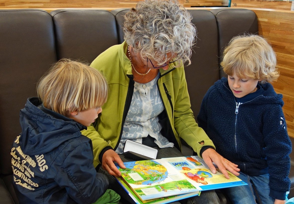 Eine Frau mit grauen Haaren liest zwei Kindern vor.